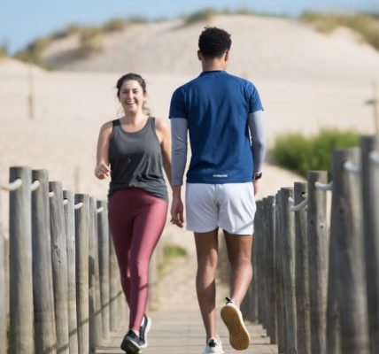 A couple enjoys jogging on a sunny beach boardwalk in Portugal, capturing a moment of fitness and leisure.