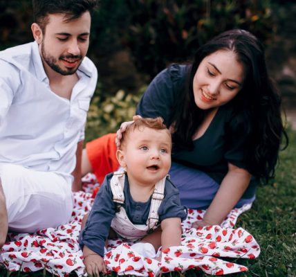 A joyful family enjoying a picnic outdoors during summer. Smiling parents with their baby on a blanket.
