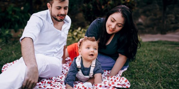 A joyful family enjoying a picnic outdoors during summer. Smiling parents with their baby on a blanket.
