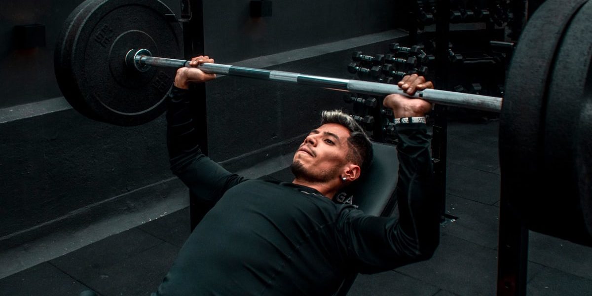 Man performing bench press with heavy barbell in a gym setting, focusing on strength training.