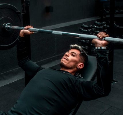 Man performing bench press with heavy barbell in a gym setting, focusing on strength training.