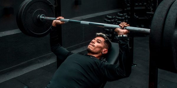 Man performing bench press with heavy barbell in a gym setting, focusing on strength training.